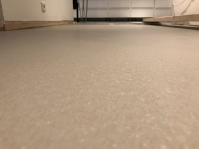 Torkat fiberarmerat flytspackel på golv i ett rum med suddiga bakgrundsobjekt.