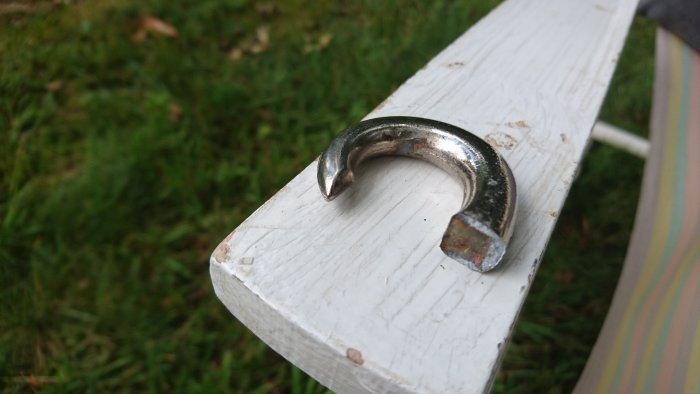 Defekt karbinhake av metall som är delvis ihålig, vilandes på en vitmålad träplanka.