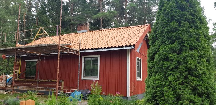 Rött hus med ny lagda takpannor och ställning runt, skorsten i dåligt skick syns uppifrån.