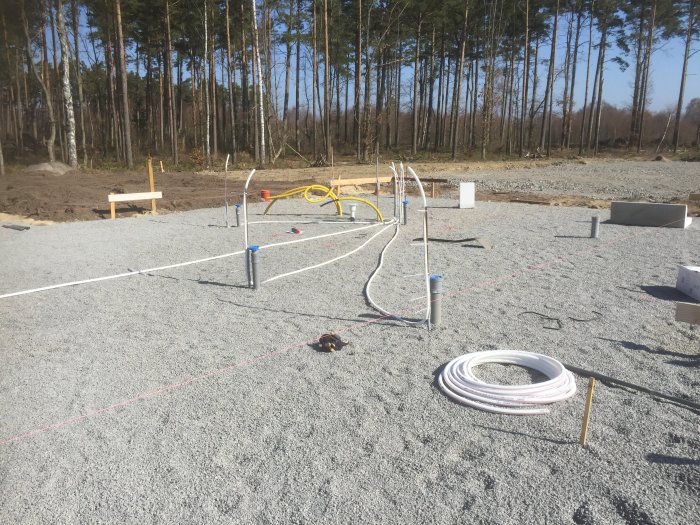 Kallvattenrör installerade i makadam på en byggplats med skog i bakgrunden.