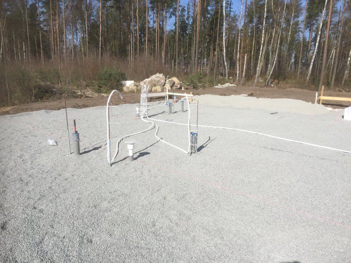 Kallvattenrör installerade i makadam på byggplats med skog i bakgrunden.