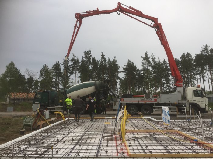 Gjutning av betongplatta med armeringsnät, betongbil och betongpump i molnigt väder.