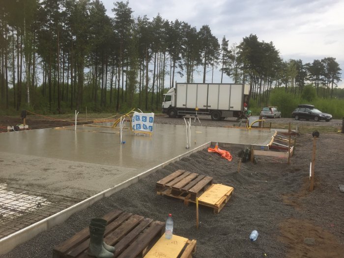 Nygräddad betongplatta på bygge med arbetsfordon och verktyg runtom, under molnig himmel.