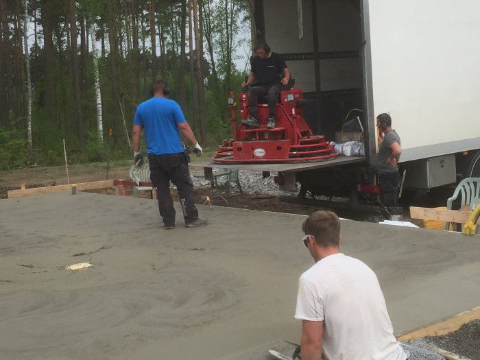 Arbetare glättar en nyligen gjuten betongplatta med maskin under molnig himmel.