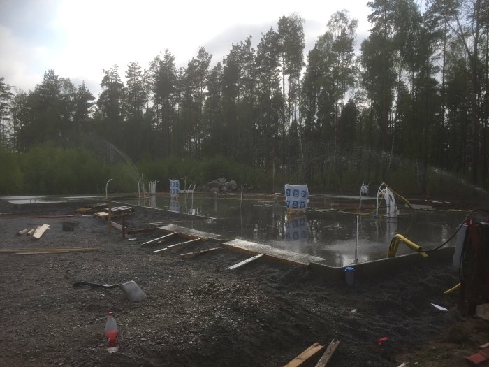 Nyglättad betongplatta för byggprojekt med skog i bakgrunden och molnig himmel.