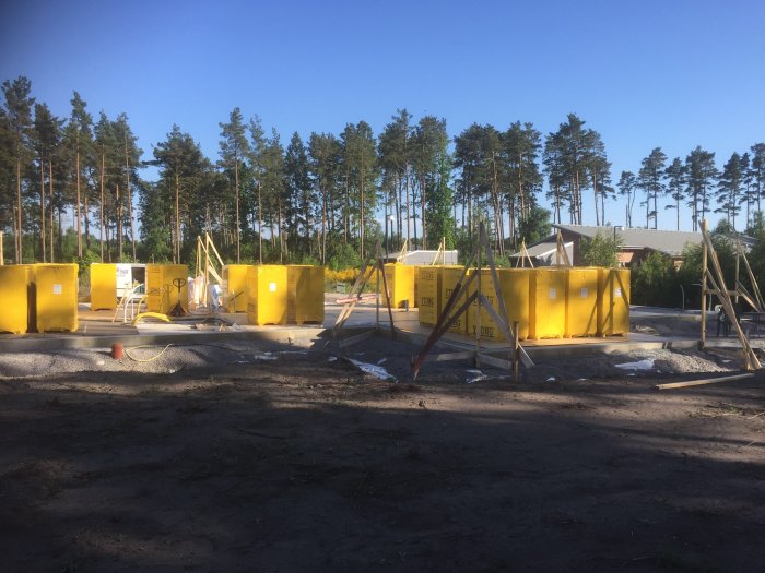 Ett byggprojekt med gula Xella Ytong block och skyddat golv på en byggplats med skog i bakgrunden.