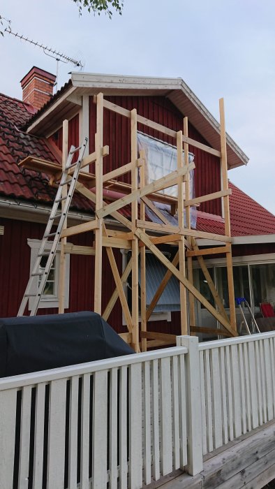 Nykonstruerad träställning på en röd husvägg med tillagd sektion och golvyta, inklusive stege och snabbtvingar.