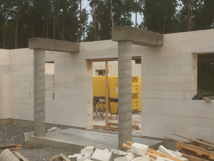 Nybyggda betongpelare och balk vid entré till hus under konstruktion, oputsade väggar och byggmaterial synligt.