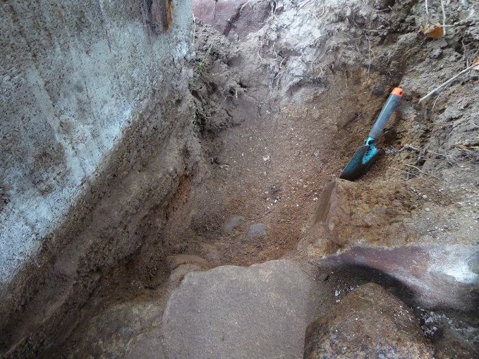 Urgrävd del av en vedbodsgrund med rensat område och en spade, redo för gjutning av en ny klack.