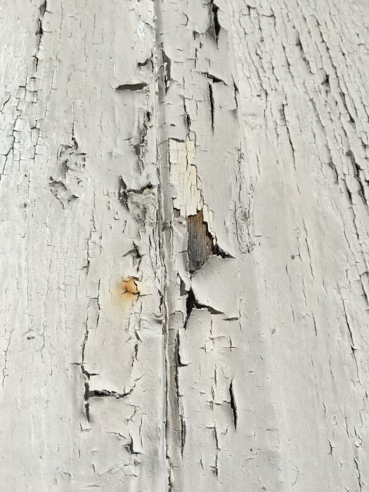 Fasad med flagande färg visar två lager av olika nyanser på ett äldre hus.