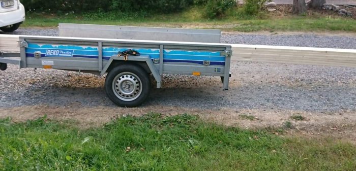 En släpvagn lastad med långa träbrädor för byggprojekt på en grusuppfart.