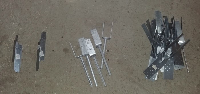 Stolpskor och gaffelankare i metall upplagda på betonggolv, skänkes från byggprojekt.