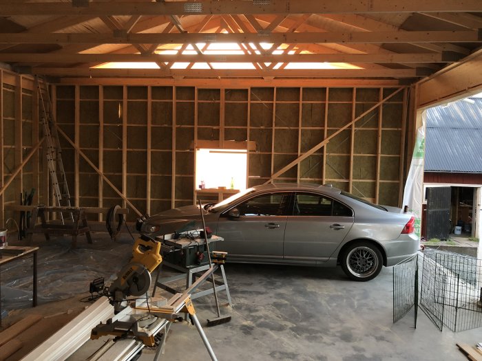 Bil parkerad i ett garage under konstruktion med verktyg och byggmaterial synliga.