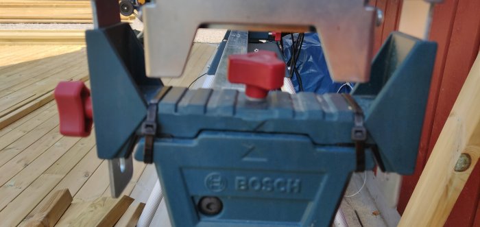 En blå Bosch-verktyg fastsatt med buntband, suddig bakgrund av träaltan.