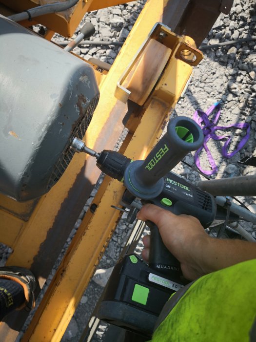 Person använder en Festool QuaDrive skruvdragare för att dra åt en skruv i en 12kW motor med bakgrund av grus och maskindelar.