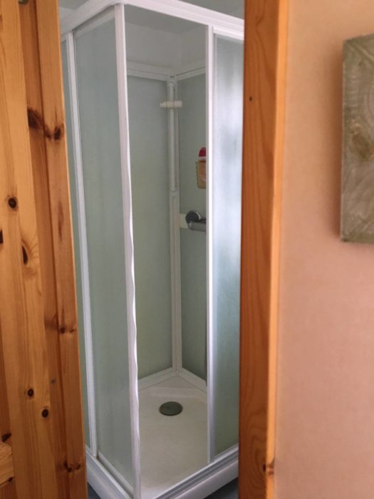 Äldre duschkabin av okänt märke i ett trångt duschrum med vita profiler och frostat glas.