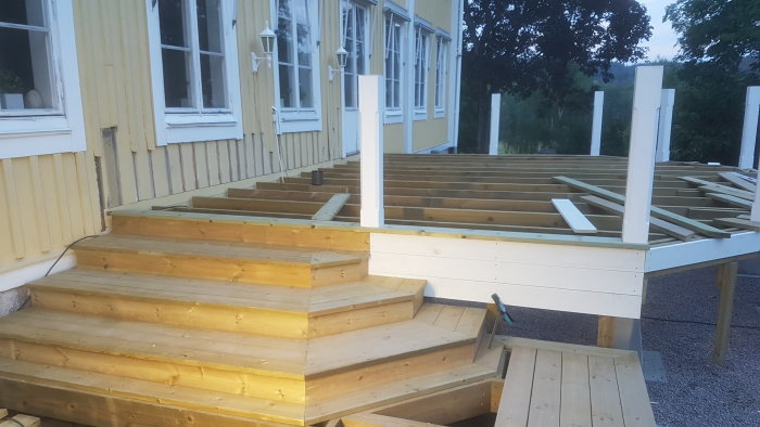 Nybyggd trätrapp som leder upp till ett halvfärdigt däck vid ett hus.