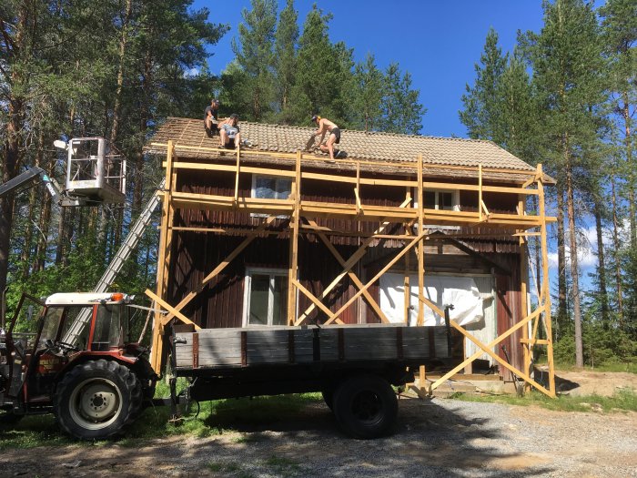 Renoveringsarbete på gång på ett äldre hus med personer som byter takpannor, stöttat av ställningar.