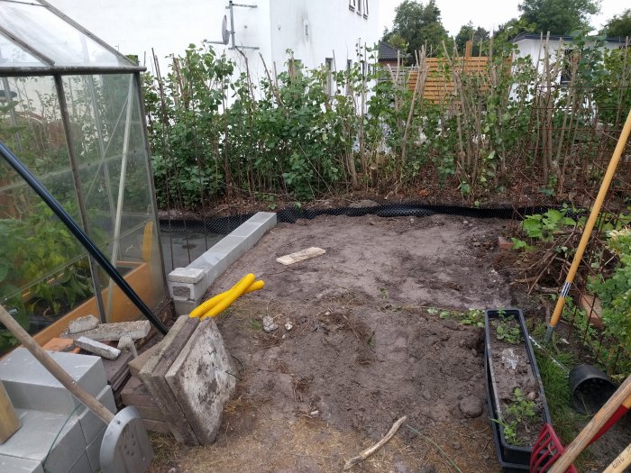 Trädgård under renovering med utrullad sättsand, stödmur av mursten och grönsaksbäddar i bakgrunden.