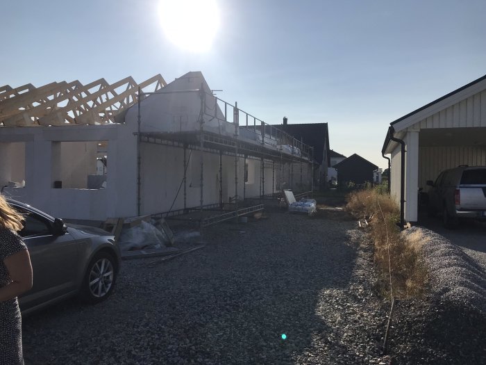 Hus i konstruktion med synligt takstolar och ställning, intill grusuppfart och befintlig carport.