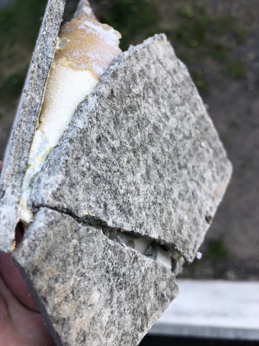 Närbild på ett brutet stycke av byggmaterial med fiberstruktur och isolering.