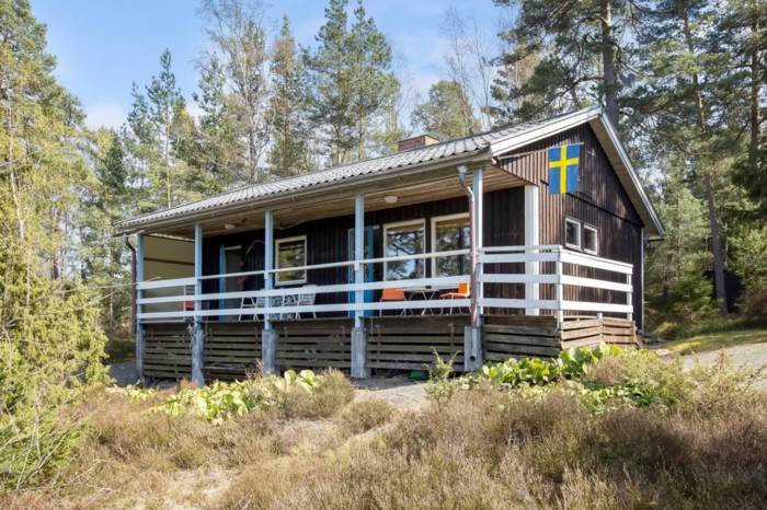 En traditionell svensk sommarstuga i skogen med en svensk flagga på verandan.