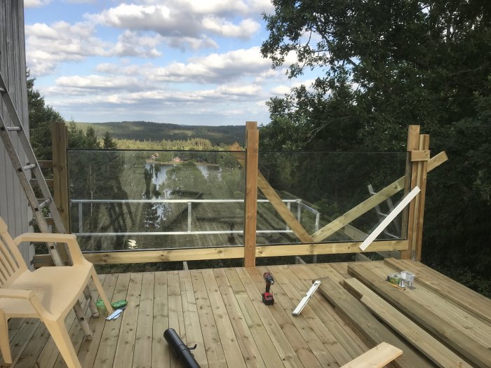 Utsikt från ett trädäck under konstruktion med förstärkt trä-räcke och kryssade stolpar, verktyg synliga på golvet.