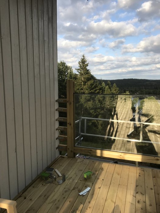 Förstärkt räcke på altan under konstruktion med verktyg och skruvar på trägolv, och monterat fönster i bakgrunden.