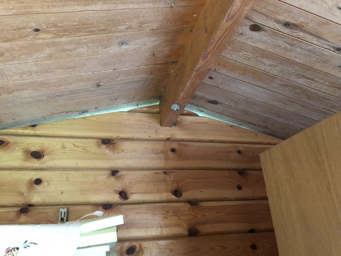 Inre hörn av en friggebod med träväggar och tak visar behovet av tilläggsisolering.