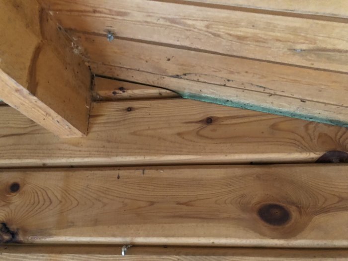 Träpanel och isolering i hörnet av ett golv i friggebod.