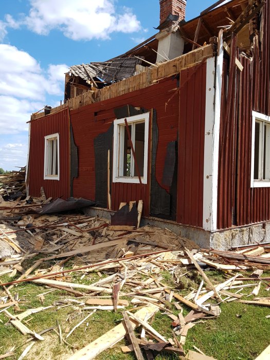 Rödfärgat hus under rivning med trasigt tak och spillror på marken.