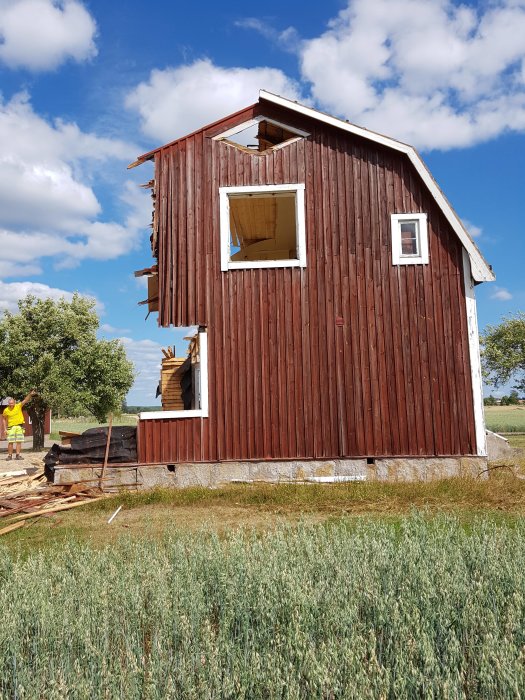 Rödfärgad stuga under rivning med delar av väggen borttagna och spillror runt omkring.
