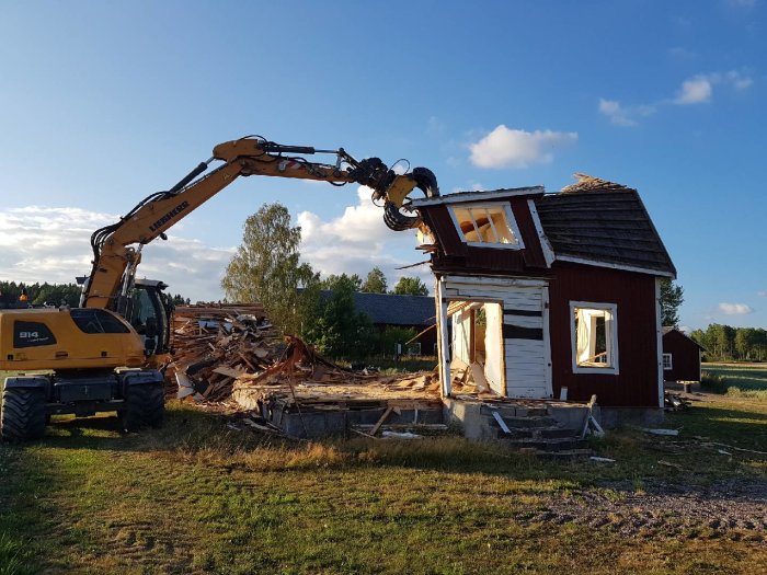 Grävmaskin som river rött hus, stora delar av byggnaden ligger redan i spillror.