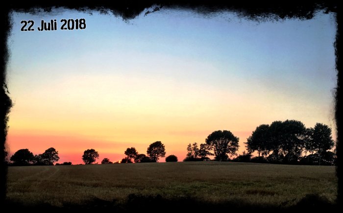 Solnedgång över ett fält med träd silhuetter och datumet 22 juli 2018 i övre vänstra hörnet.