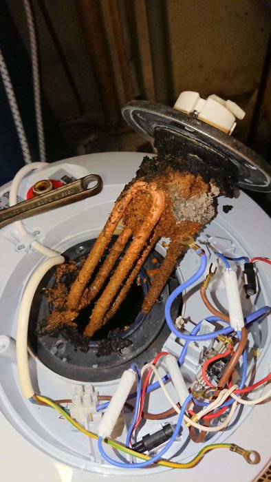 Inuti en varmvattenberedare med kraftiga kalkavlagringar och korrosion på värmeelementen.