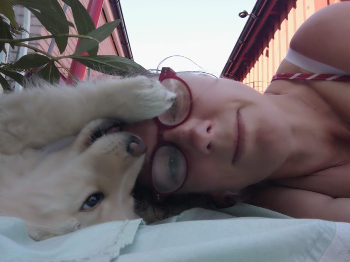 Kvinna ligger på rygg utomhus med en lekfull golden retriever-valp ovanpå sig.