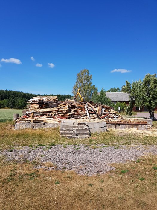 En hög med rivningsavfall bestående av träplankor och betongblock under en klarblå himmel, redo att fylla containrar.