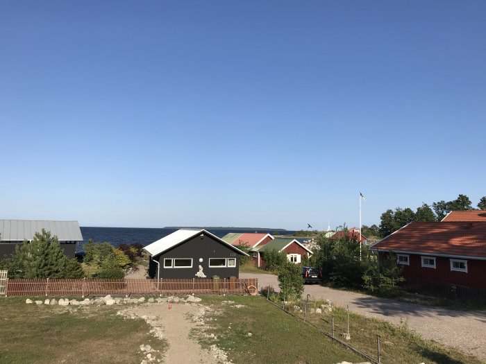 Klart blå himmel över en kustby med traditionella hus och svensk flagga.