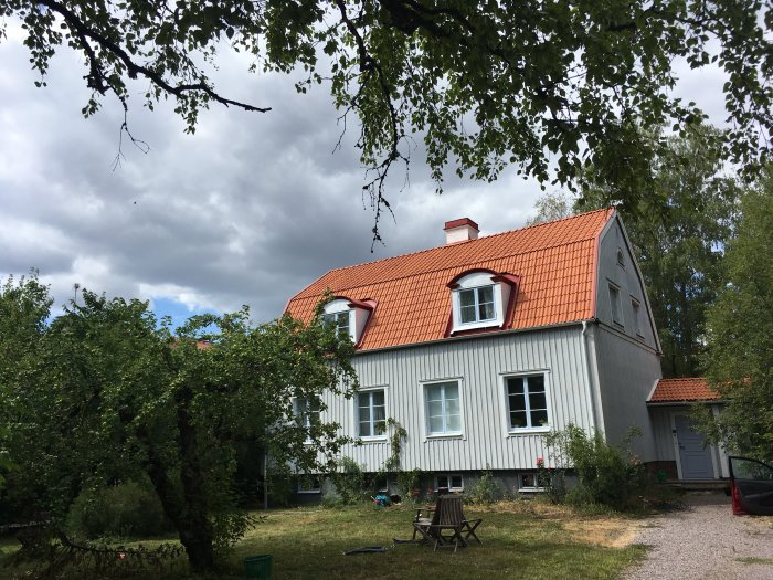 Nyrenoverat Vittinge lertegeltak på ett vitt hus med två våningar och röda takfönster i en lummig trädgård.