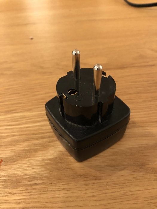 Adapter för elektrisk kabel med tre stift ovanpå en bordsskiva.