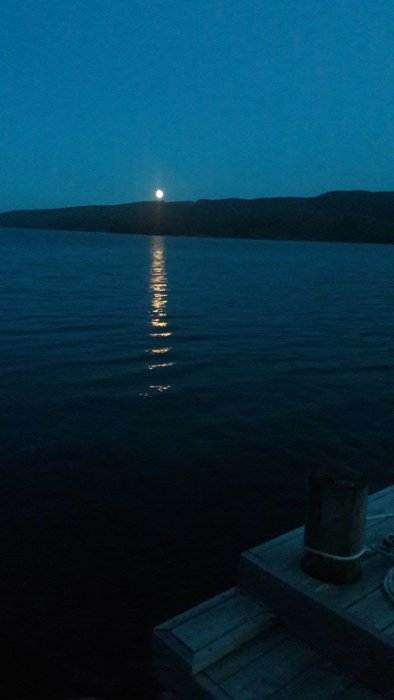 Månen lyser över vatten vid Skuleskogens nationalpark från en mörk himmel, reflektion i vattnet.