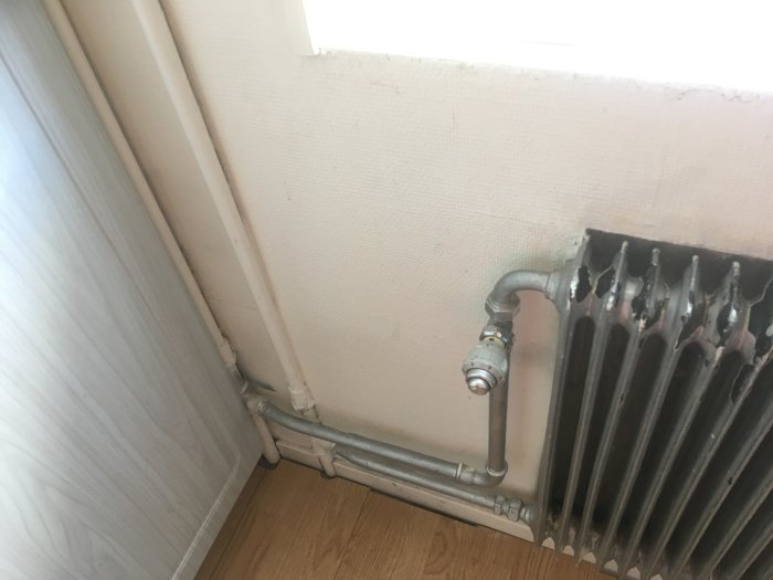 Radiator med silvermålade rör och en termostat vid en vägg, rörsträckning behöver pluggas för renovering.