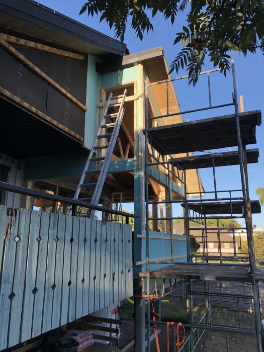 Hus under renovering med nymonterad utegips och byggnadsställning, klarblå himmel i bakgrunden.