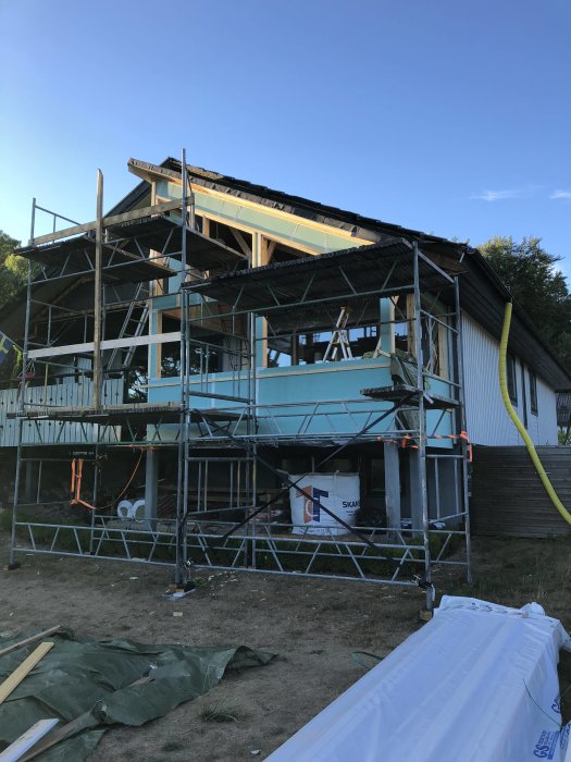 Hus under renovering med nytt utegips, ställningar runtom och byggmaterial på marken.