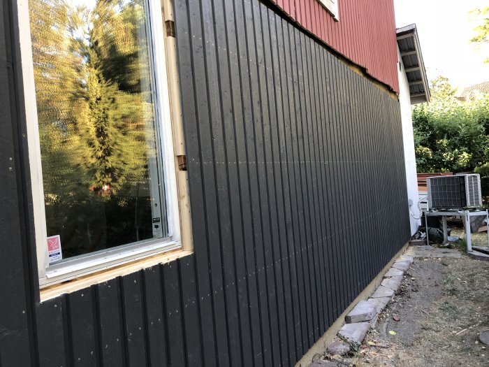 Ny monterade träpaneler på väggen av ett hus, befintligt litet fönster synligt, målning i arbete.