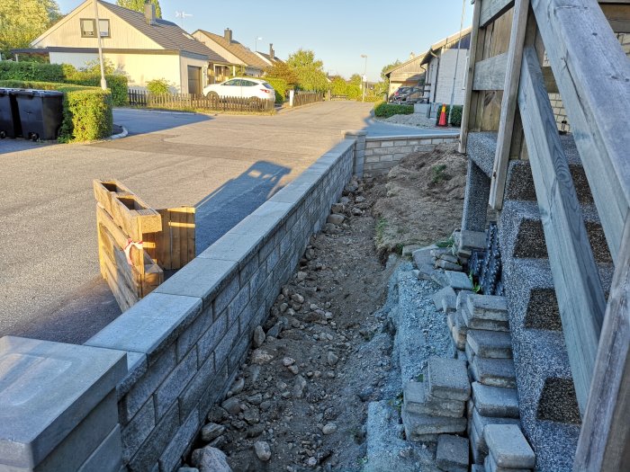 En pågående murkonstruktion med oplacerade stenblock och grus längs en trädgårdsväg.