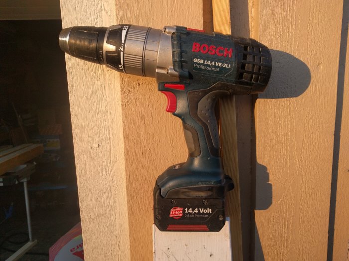 En begagnad Bosch GSB 14.4 VE-2LI borrskruvdragare upphängd på en trävägg i solnedgången.