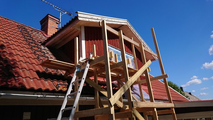 Utbyggnad av hus med trästomme och stegar under en solig himmel.