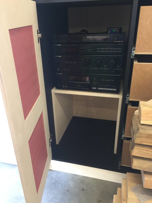 Stereoanläggning installerad i hyllsektion med öppen dörr och trästycken i förgrunden.