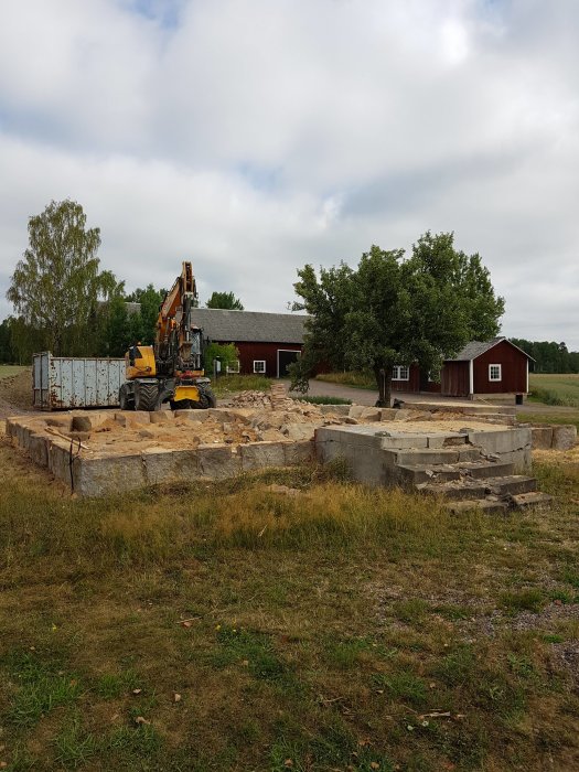 Grävmaskin vid en byggarbetsplats med en betonggrund och utspritt sågspån.